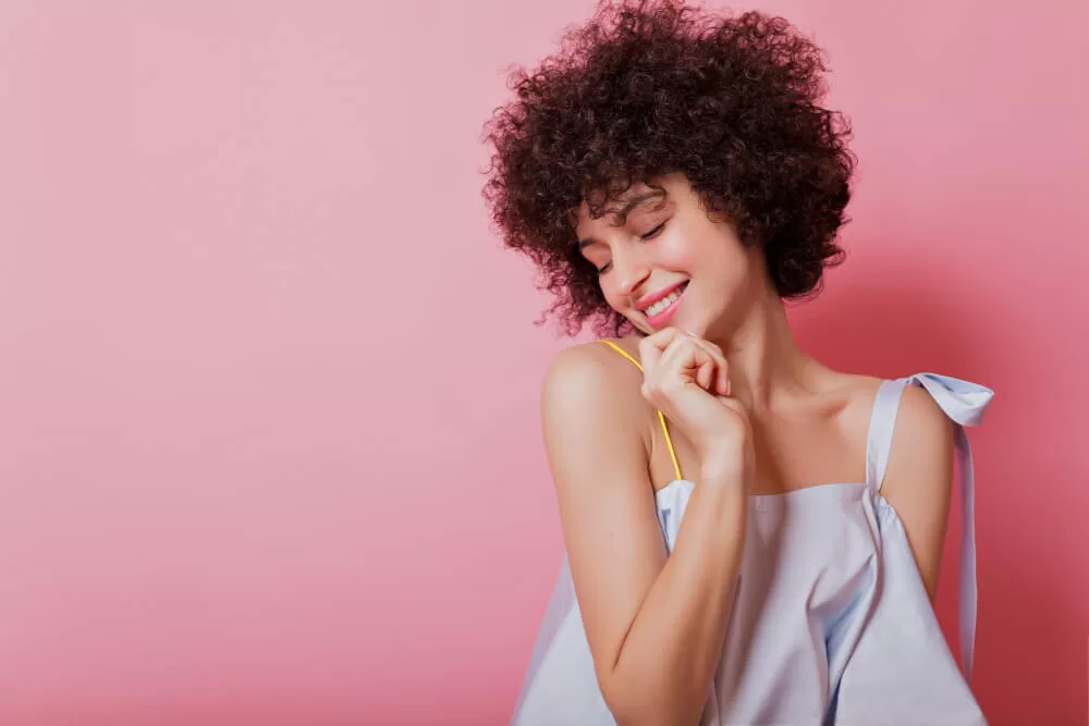 mulher com cabelo cacheado bem hidratado e bonito em um fundo rosa