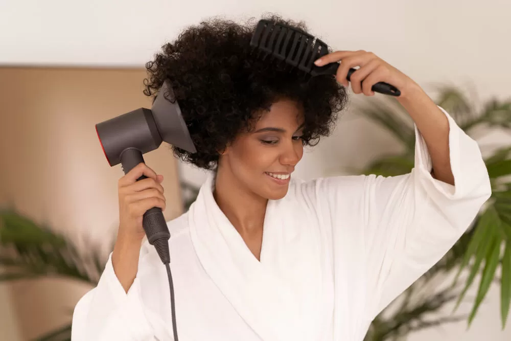 mulher de cabelos cacheados volumosos secando seu cabelo com secador